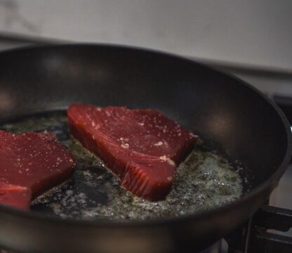 Two-raw-deep-red-tuna-steaks-frying-in-butter-and-oil-in-black-frying-pan